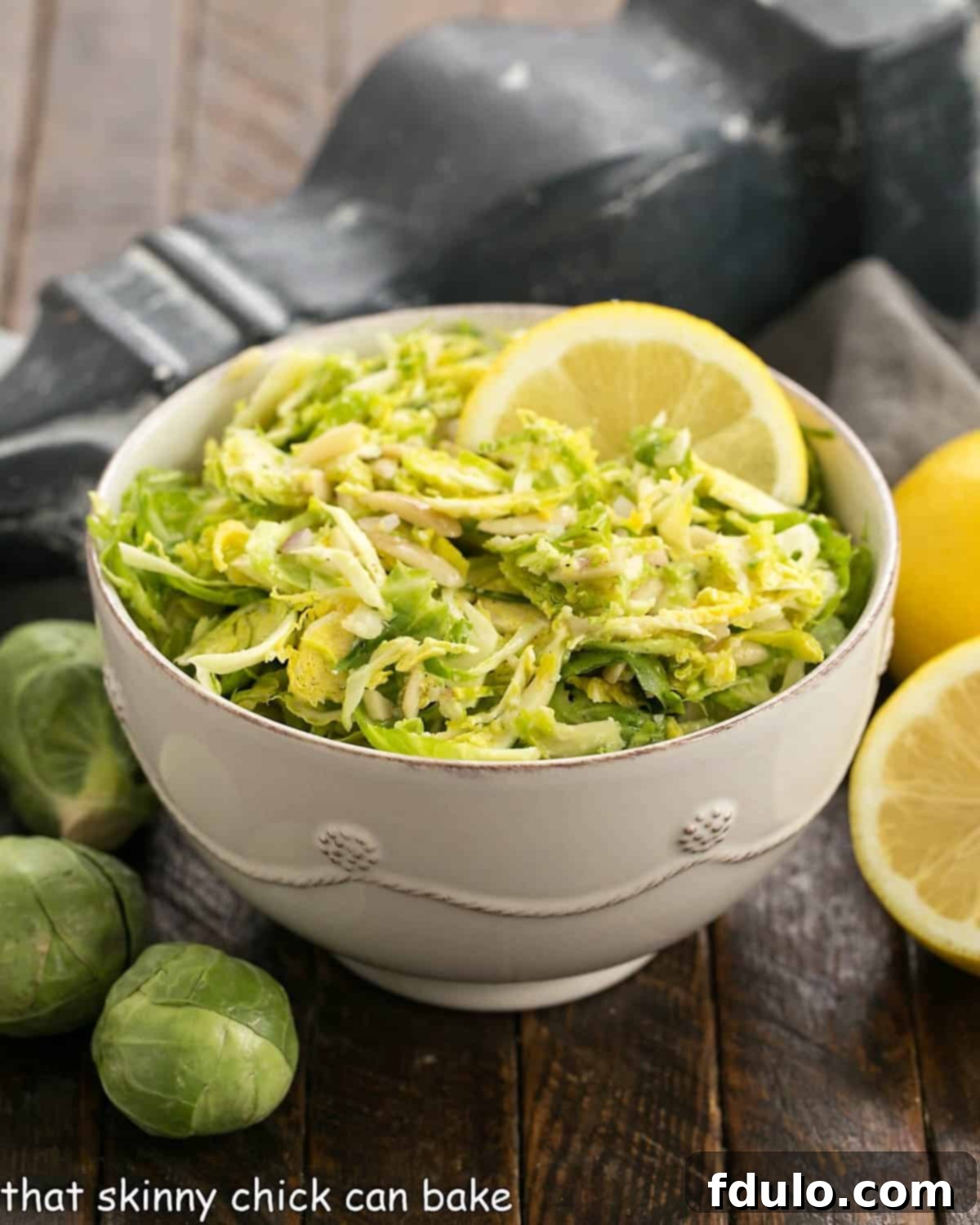A close-up side view of a generous serving of Shaved Brussels Sprouts Salad in a white ceramic bowl, highlighting the delicate texture and vibrant dressing.