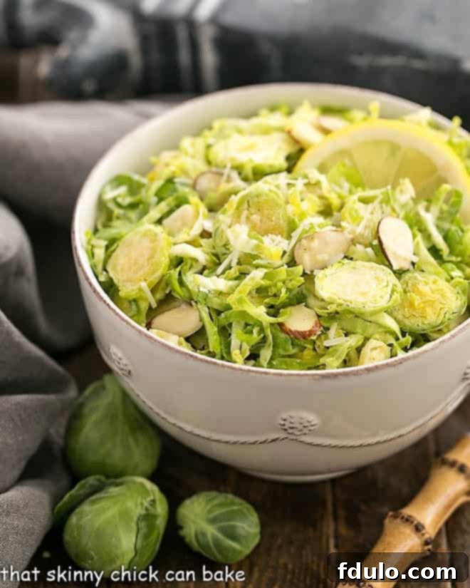 A pristine white salad bowl filled with Shaved Brussels Sprouts Salad, garnished with a fresh lemon slice and a bamboo-handled fork, ready to be enjoyed.