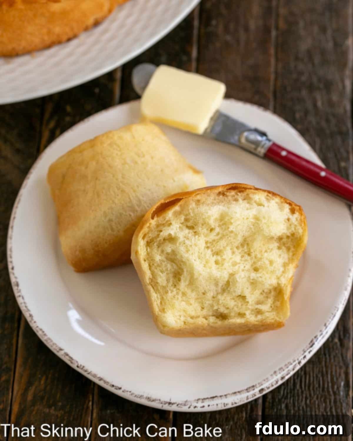 Soft and Fluffy Japanese Milk Bread 3 A Japanese Milk Bread Bun perfectly torn in half on a small white plate, revealing its incredibly soft, fluffy, and feathery interior, accompanied by a small red butter knife.