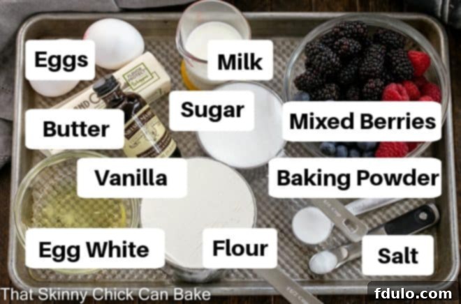 Various labeled ingredients for a berry cake laid out neatly on a metal sheet pan, including flour, sugar, butter, eggs, and a selection of fresh berries.