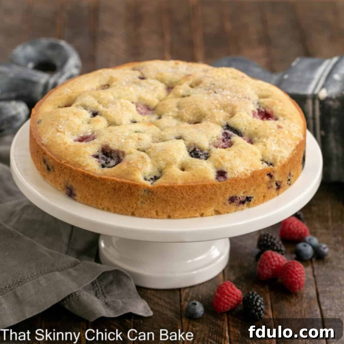 A beautiful one-layer cake topped generously with mixed fresh berries, displayed on a elegant cake stand.