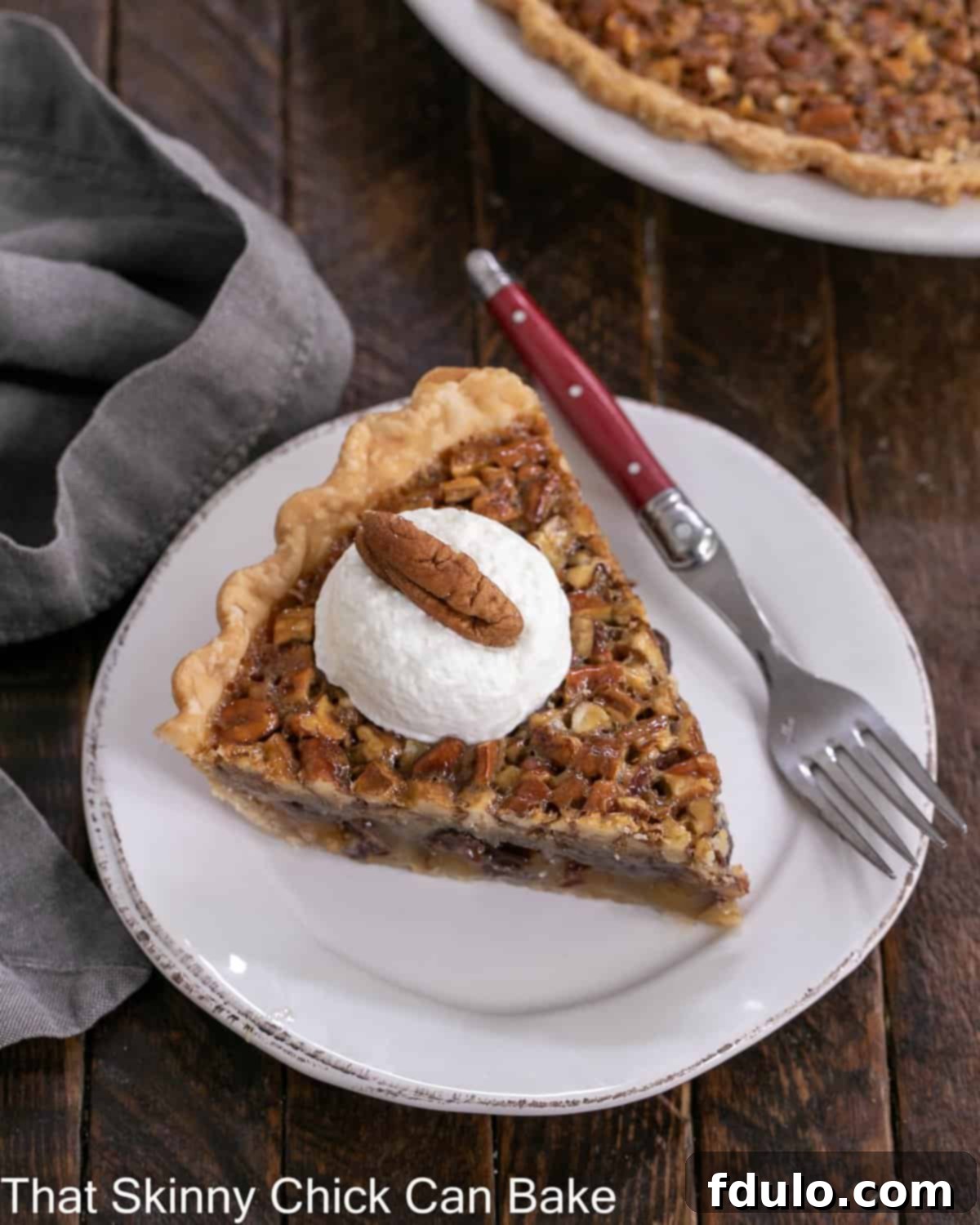 Overhead view of a slice of Derby pie topped with whipped cream and a pecan on a white dessert plate, showcasing its rich texture.