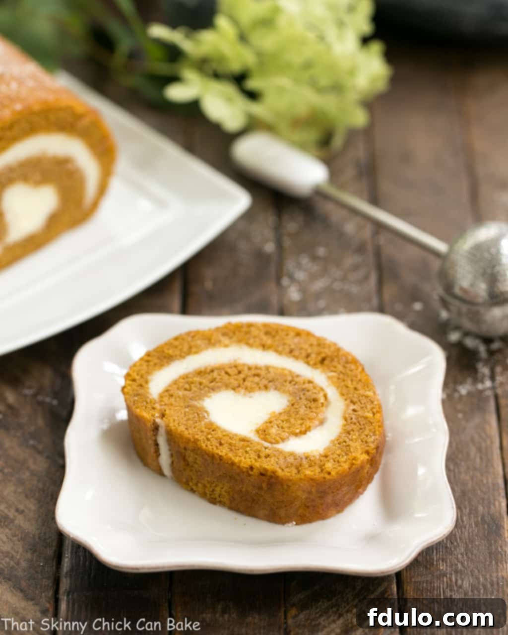 A slice of Old Fashioned Pumpkin Roll on a white plate, showcasing the cream cheese swirl.