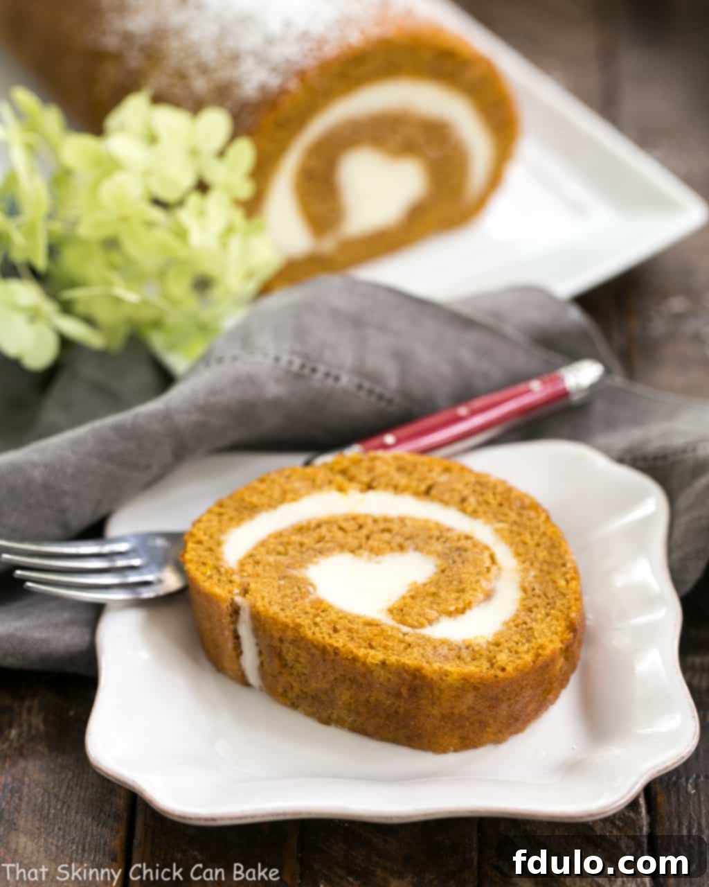 A perfectly sliced old-fashioned pumpkin roll revealing the creamy swirl, served on a white ceramic plate.