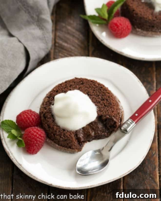 Chocolate Lava Cakes -Individual Chocolate Cakes with a molten hot, oozy chocolate filling! Overhead with of a chocolate lava cake topped with Kahlua whipped cream on a white plate with a raspberry and mint garnish and a red handle spoon