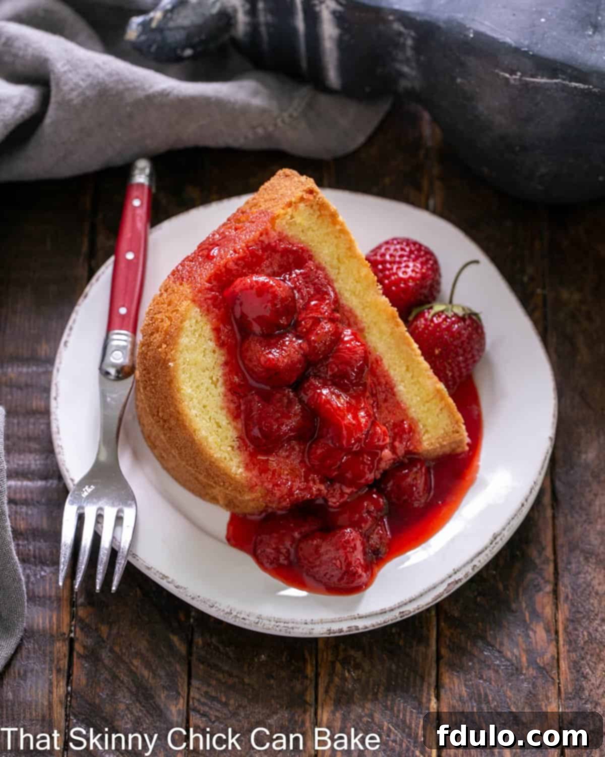 Overhead view of a slice of lemon bundt cake topped with strawberry coulis on a white dessert plate.