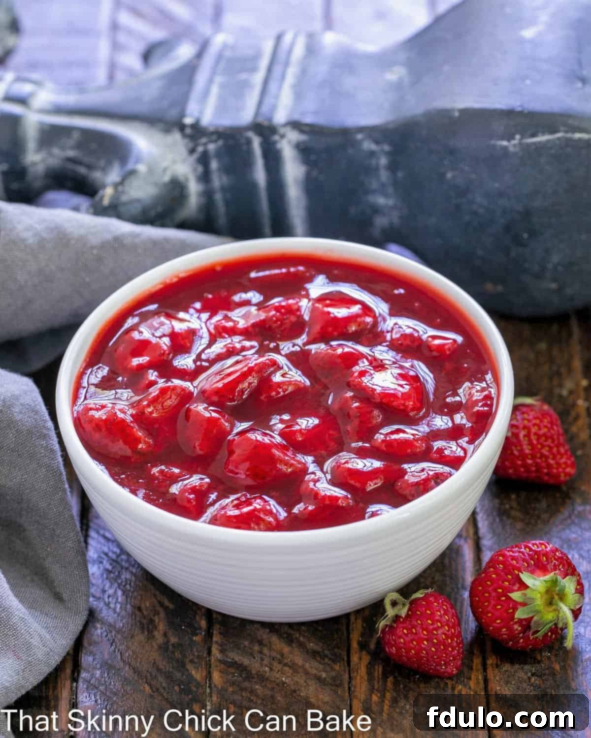 A white bowl full of strawberry sauce with a few fresh strawberries on the side.