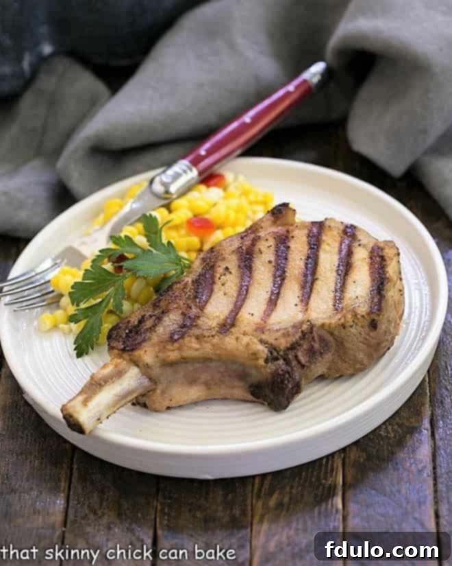 A perfectly grilled marinated pork chop resting on a dinner plate, accompanied by fresh corn on the cob and a red-handled fork.