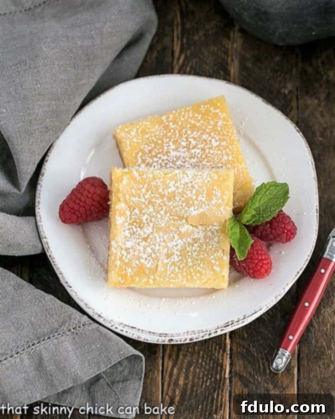 Overhead view of glistening slices of homemade gooey butter cake on a white plate, garnished with fresh raspberries.