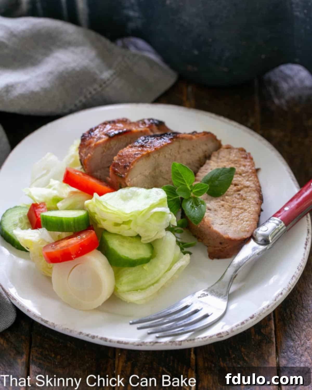 Slices of grilled pork tenderloin with a green salad and a red handled fork on a white ceramic plate.