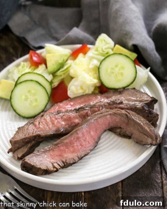Easy Marinated Flank Steak slices on a white plate, garnished with fresh herbs.