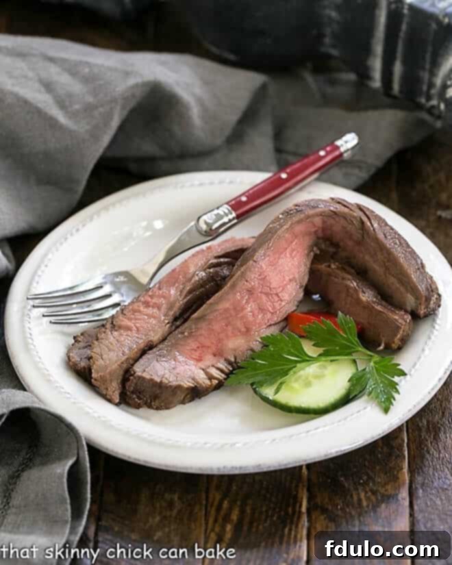 Slices of perfectly grilled flank steak on a white plate with a red handled fork, inviting a taste.