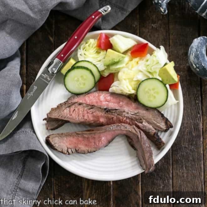 Overhead view of marinated flank steak slices on a white plate with a side of tossed salad, ready to eat.