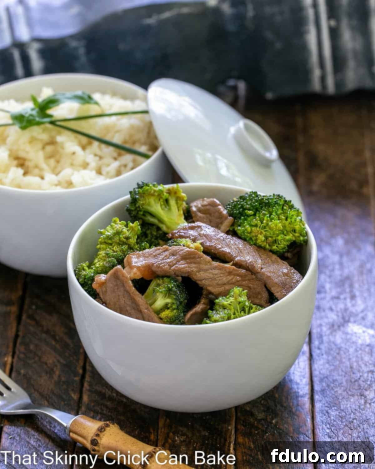 Beef stir fry recipe in a white bowl in front of a bowl of rice.