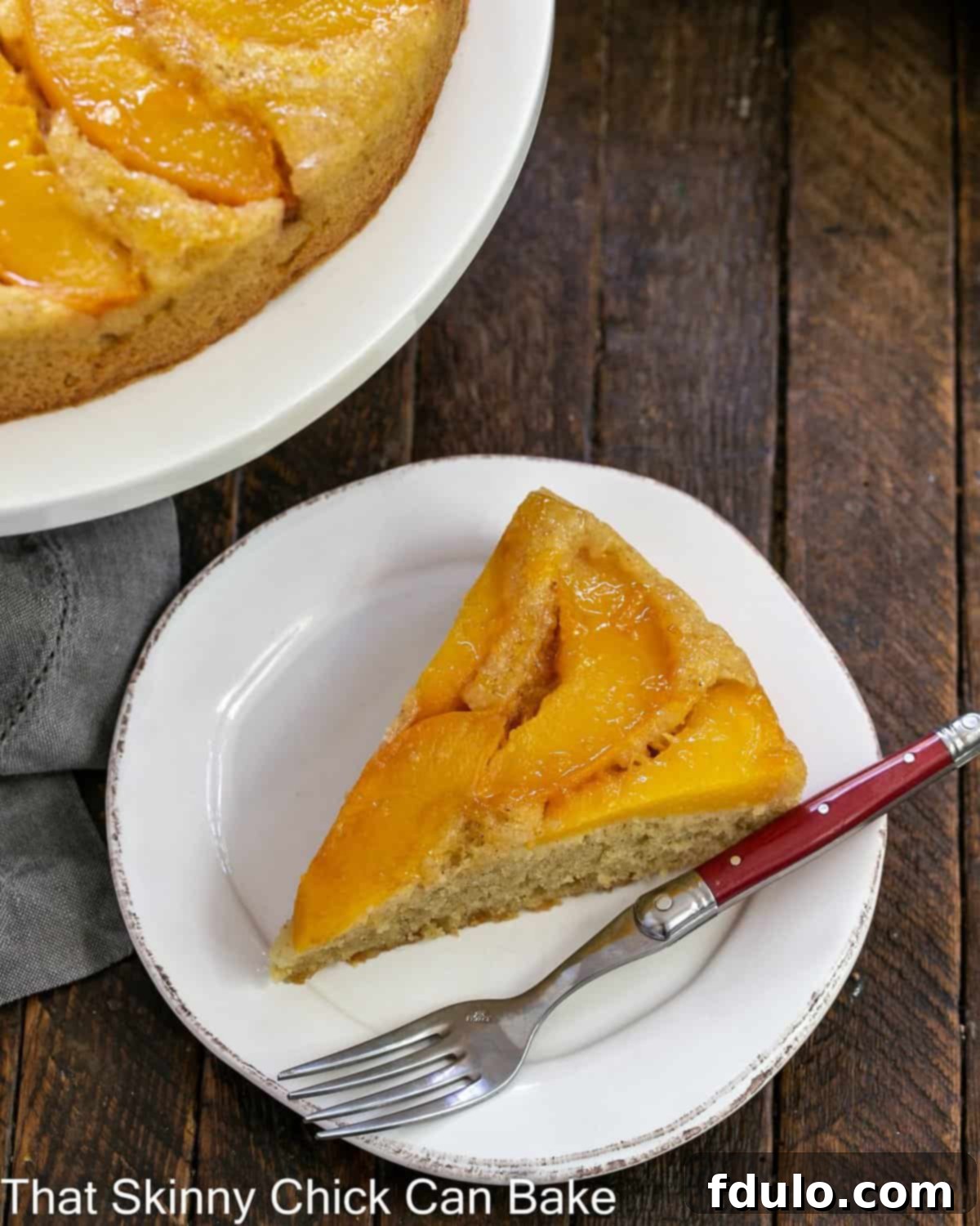 A beautifully presented slice of upside down cake with golden caramelized peaches on a white dessert plate, viewed from directly above.