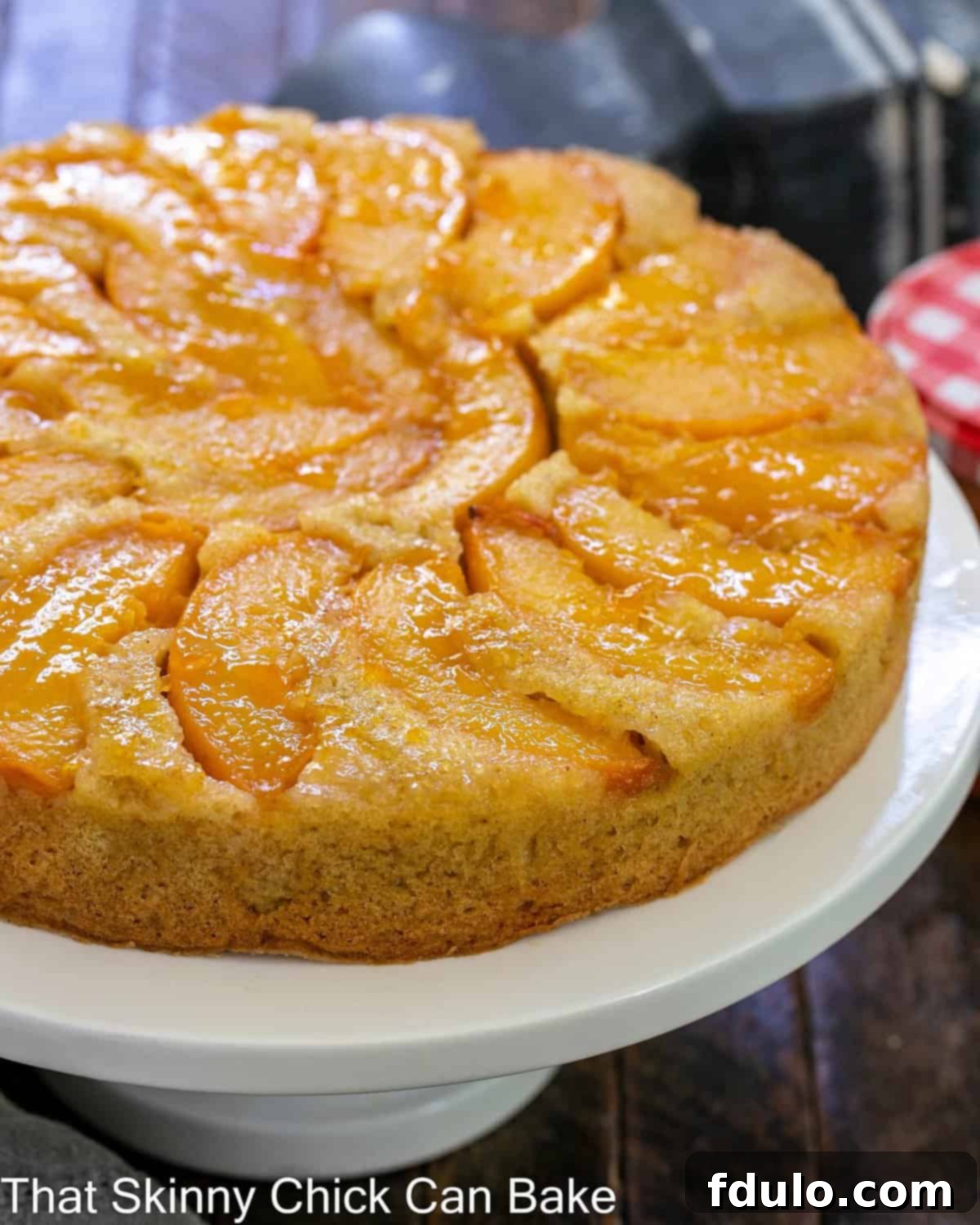 A whole peach upside down cake beautifully displayed on a white ceramic cake stand, ready to be sliced and served.
