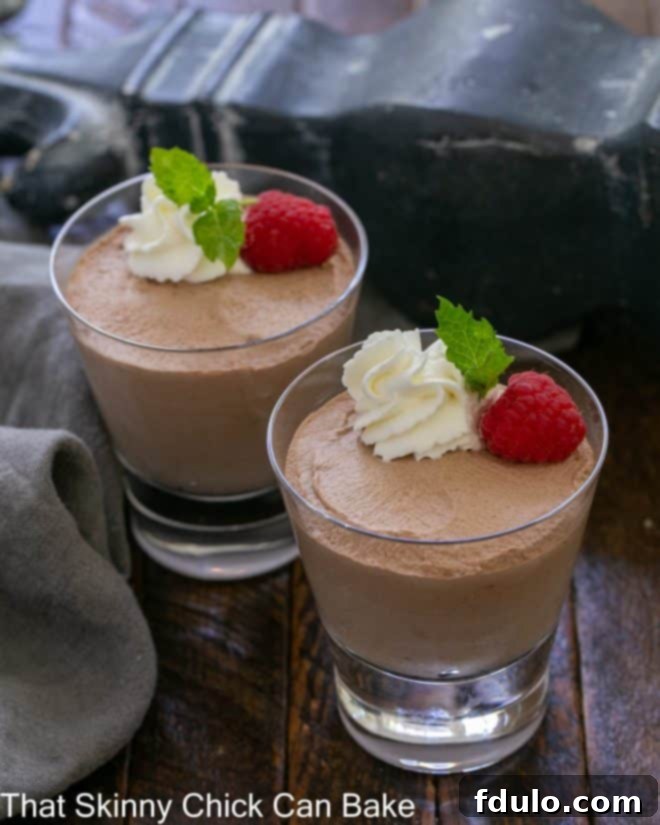 Two delicate dishes of 5-Minute Whipped Chocolate Mousse elegantly garnished with fresh whipped cream, vibrant raspberries, and a sprig of mint, showcasing its tempting texture and presentation