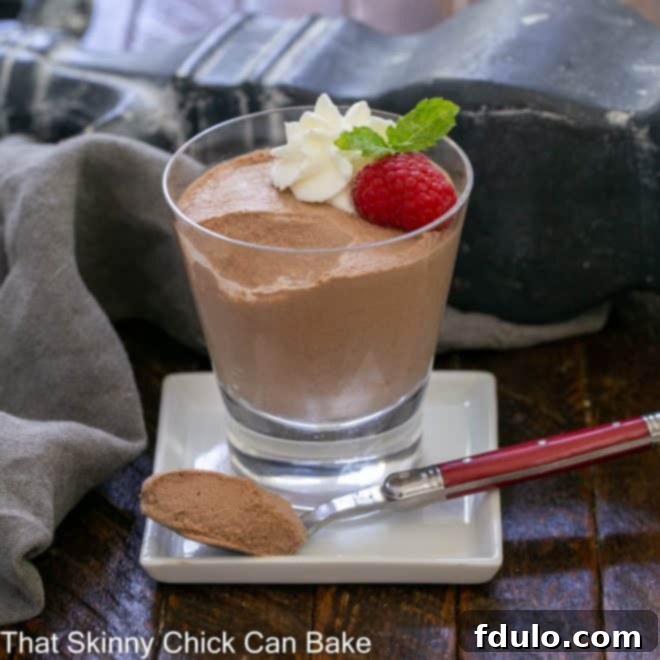 A perfectly portioned serving of rich chocolate mousse in a glass, with a spoonful carefully removed and held on a red-handled fork, inviting a taste of its creamy texture.
