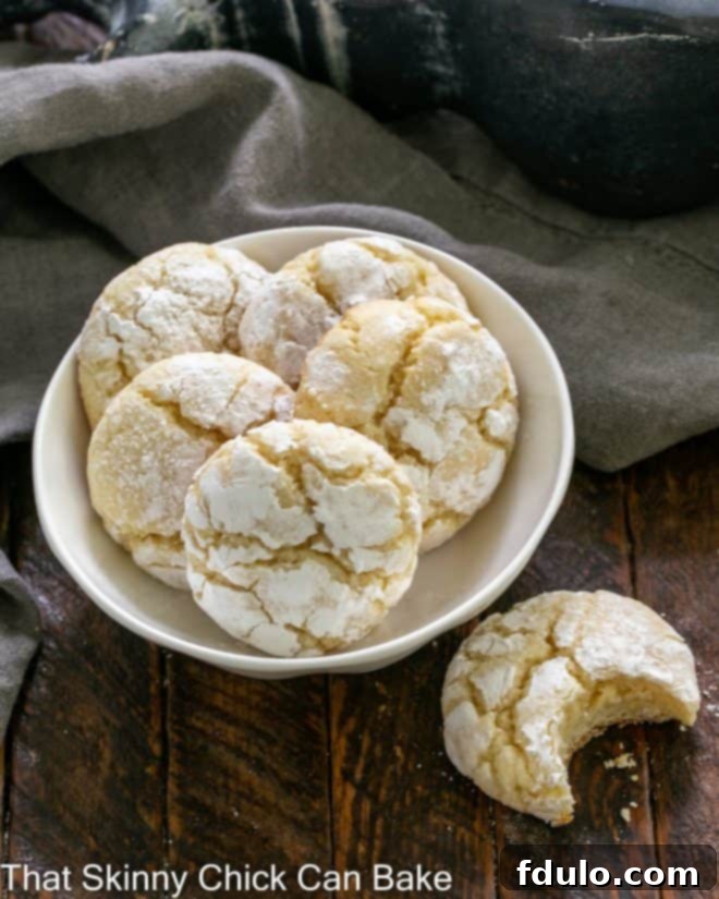 An overhead shot of a small white bowl holding five delicate Gooey Butter Cookies, with one cookie placed to the side, a bite taken out, revealing its soft, rich interior.