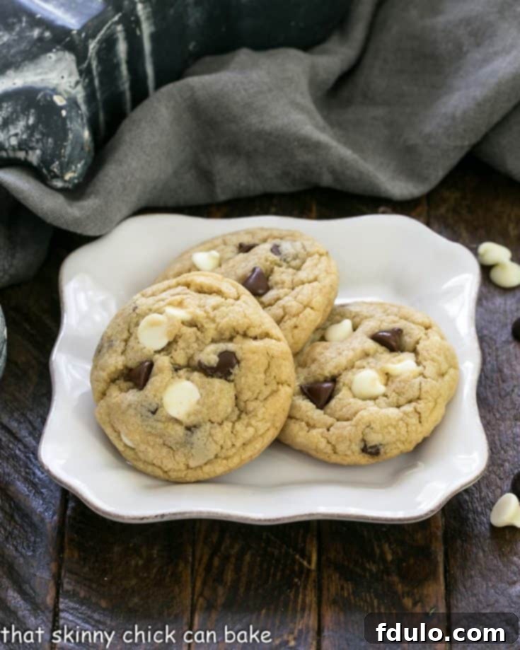 Three perfectly baked chocolate chip cookies with pudding on a square white plate, with a slightly blurred background.