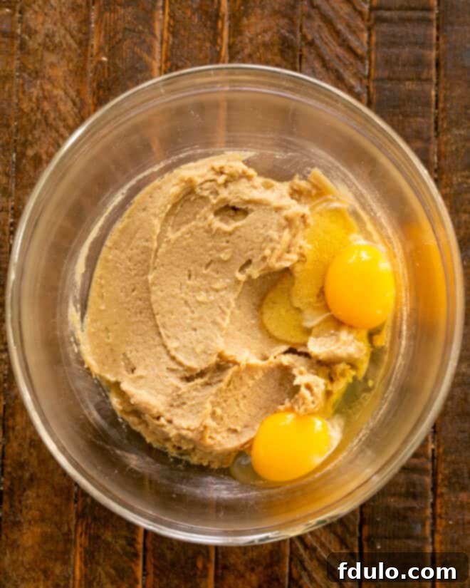 Process shot showing softened butter, granulated sugar, dark brown sugar, instant pudding mix, eggs, and vanilla extract being combined in a stand mixer.