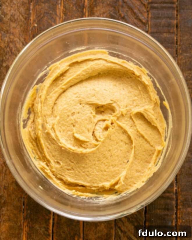 Cookie dough with dry ingredients partially incorporated, showing a fluffy texture before chocolate chips are added.