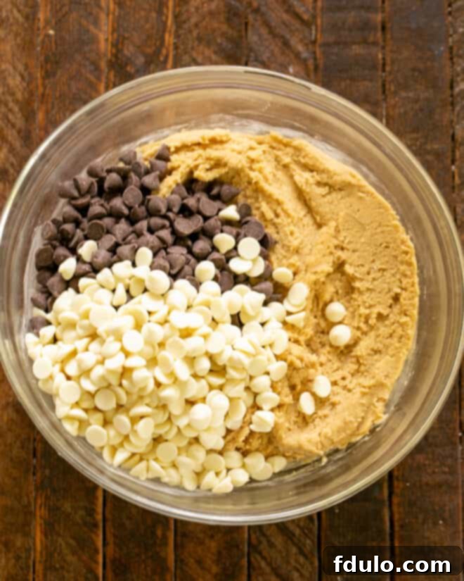 Chocolate chips being folded into the prepared cookie dough in a mixing bowl.