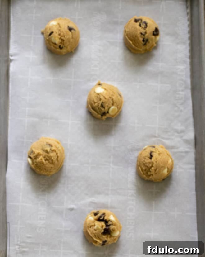 Scooped cookie dough balls placed evenly on a parchment-lined baking sheet, ready for the oven.