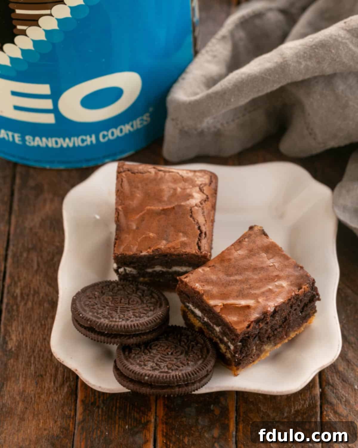 Chocolate Chip Oreo Brownies 2 Two irresistibly rich Chocolate Chip Oreo Cookie Brownies on a pristine white dessert plate, artfully garnished with two whole Oreo cookies, highlighting the delicious layers within.