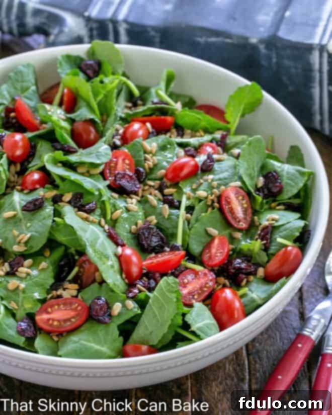 Vibrant kale salad with ruby red cranberries, halved grape tomatoes, and crunchy sunflower seeds elegantly presented in a large white serving bowl.