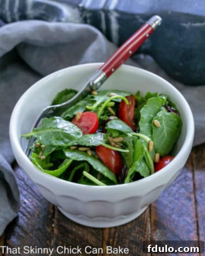 A small white bowl generously filled with vibrant kale salad, featuring a red-handled fork nestled within, ready to be enjoyed.