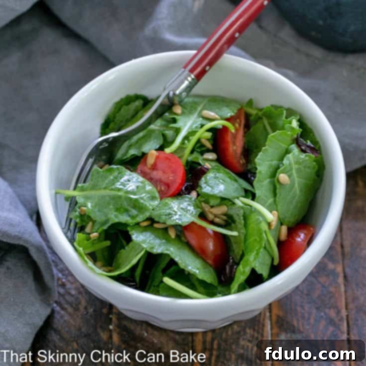 Overhead view of a small salad bowl filled with kale salad with a red handle fork.