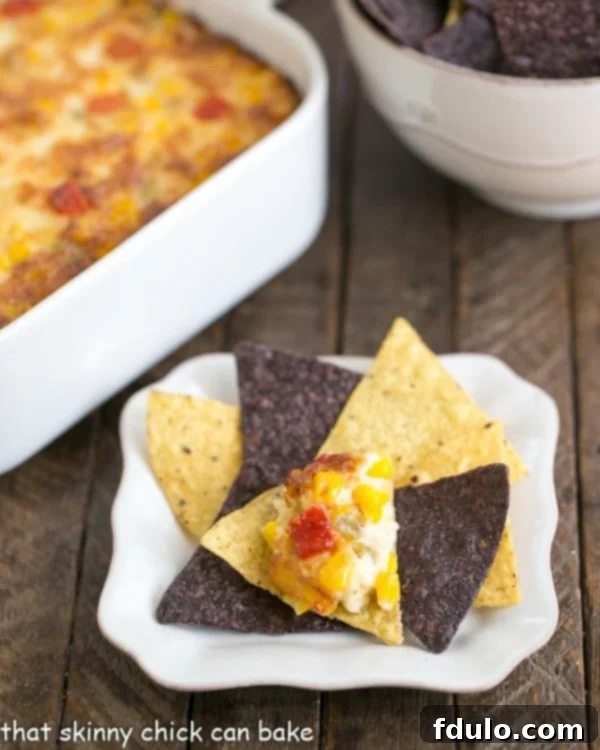 Fiesta Corn Dip - With a double dose of gooey cheese, you'll want to serve this magnificent dip at every gathering! A close-up shot of a creamy, golden Fiesta Corn Dip on a tortilla chip, invitingly presented on a white surface.