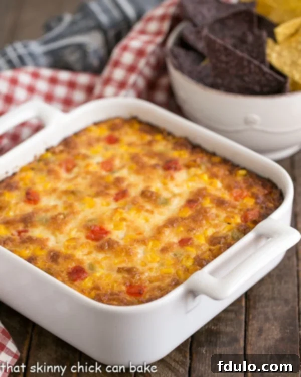 Fiesta Corn Dip - With a double dose of gooey cheese, you'll want to serve this magnificent dip at every gathering! Fiesta Corn Dip generously served in a square white casserole dish, ready to be enjoyed.