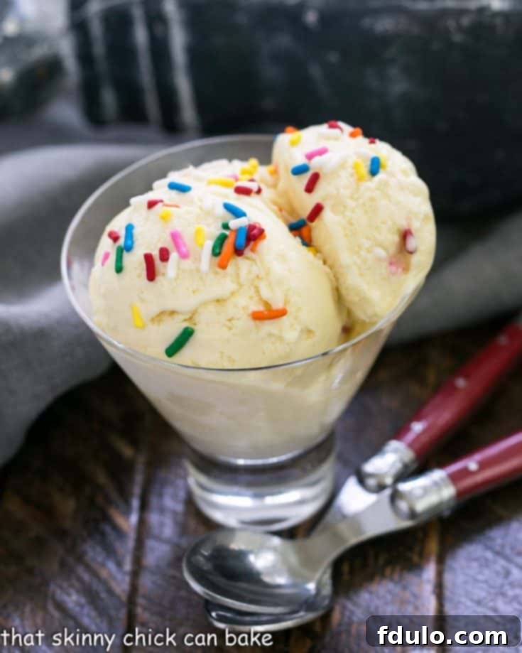 Two scoops of homemade cake batter ice cream in a glass dish with two red handled spoons, ready to be enjoyed.
