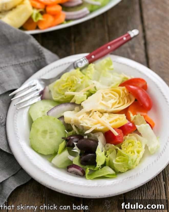 A vibrant Kitchen Sink Chopped Salad, beautifully presented on a white salad plate with a red-handled fork, ready to be enjoyed.