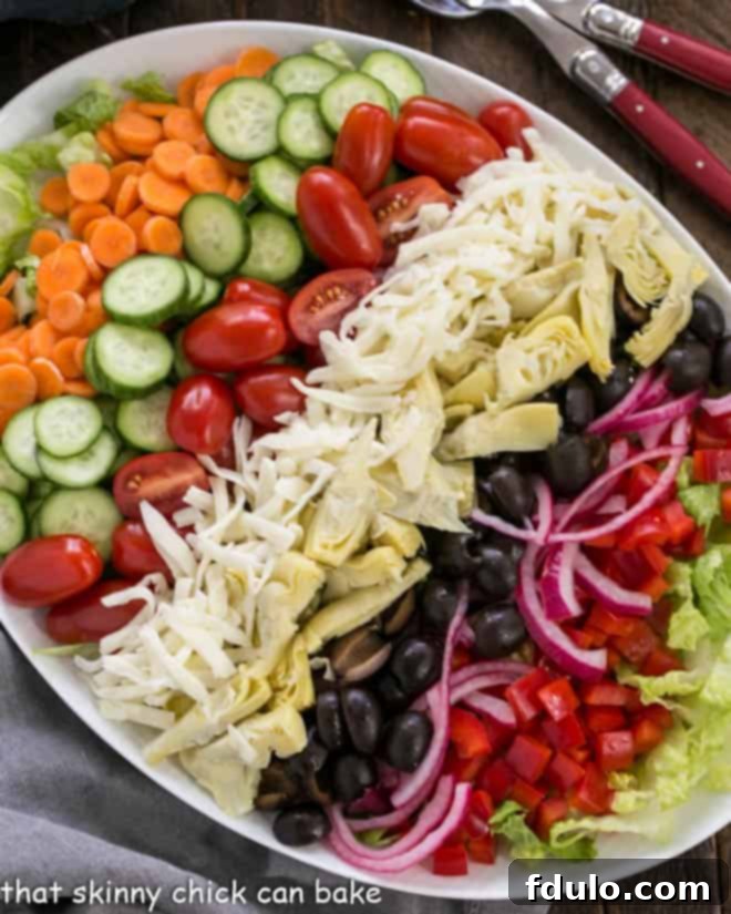 An overhead view captures a beautifully composed Kitchen Sink Chopped Salad on an oval white ceramic platter, emphasizing its fresh ingredients and vibrant colors.