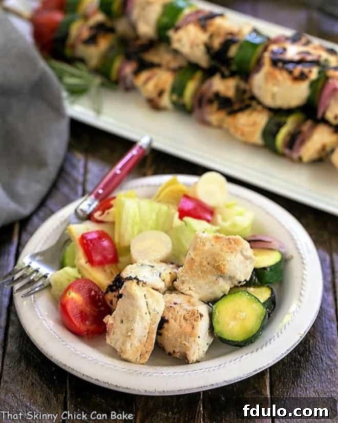Feta Chicken Kabobs served alongside a fresh green salad on a white plate, showcasing a delightful meal.