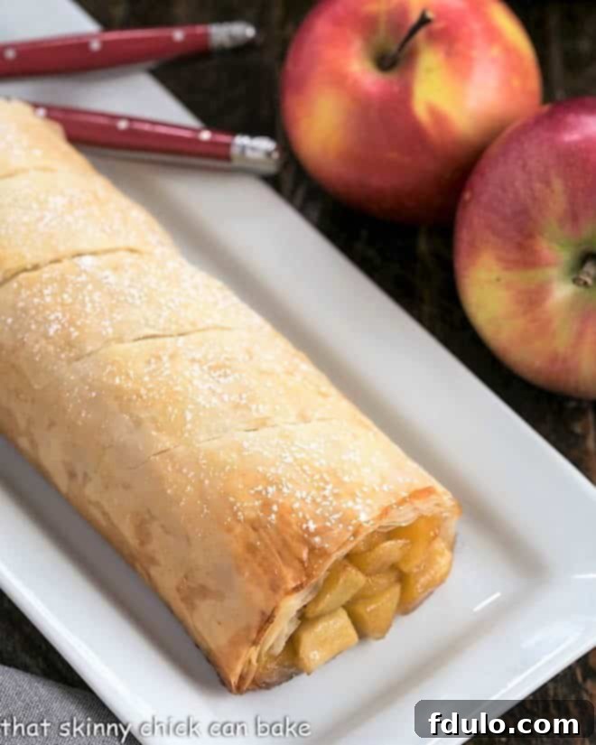 Apple Strudel with Phyllo is flaky, delicious and filled with sweet, cinnamon-spiced apples Apple Strudel lightly dusted with powdered sugar, presented on an elegant white platter.
