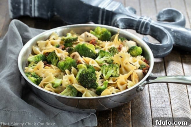 Close-up of the delicious Chicken with Broccoli, Sun-dried Tomatoes and Bow Tie Pasta simmering in a stainless steel frying pan, ready to be served.