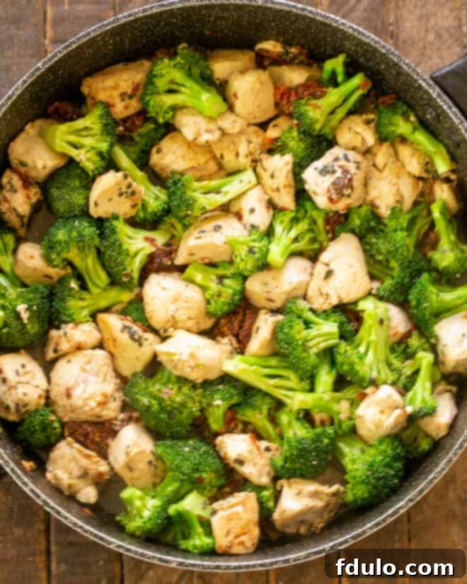 Close-up of chicken in a skillet with bright green broccoli florets, deglazed with white wine and simmering in chicken broth, creating a flavorful base for the pasta.