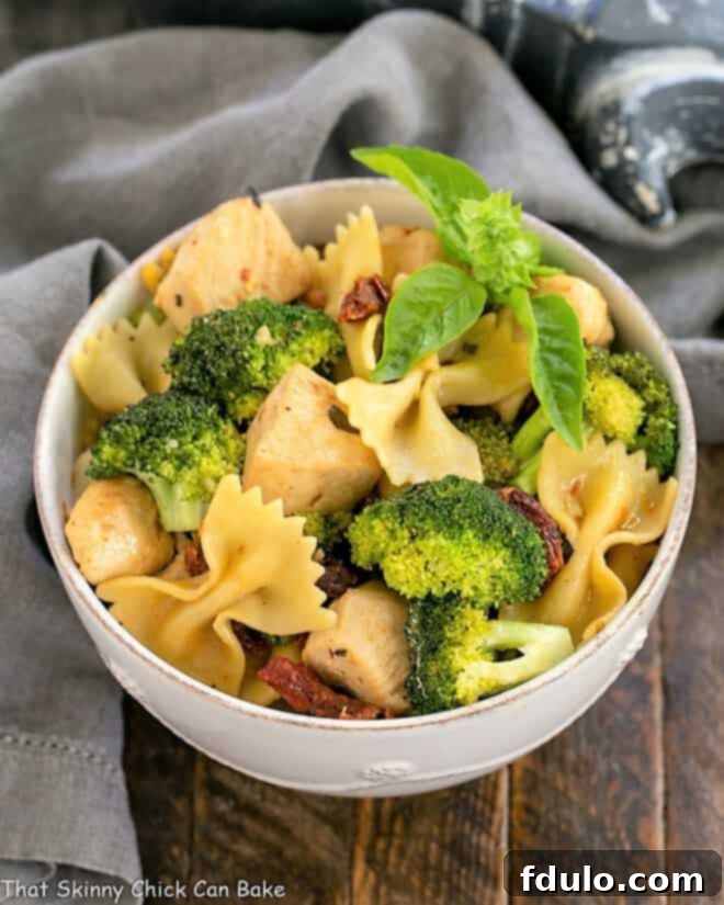 Overhead view of Chicken with Broccoli, Sun-dried Tomatoes and Bow Tie Pasta in a white ceramic bowl, garnished and ready to serve.