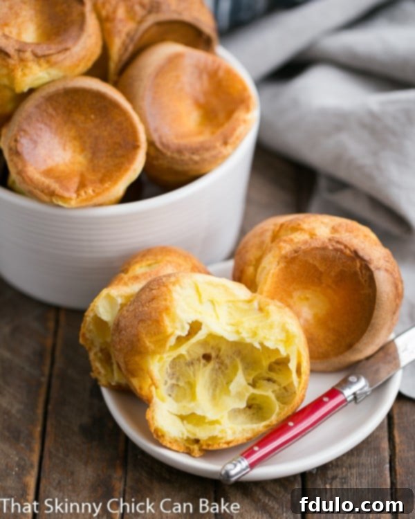 Perfect Popovers on a white plate with a small red handled knife, showcasing their golden-brown crust and impressive height.