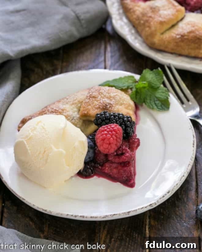 Slice of berry galette on a round white plate with a scoop of vanilla ice cream.