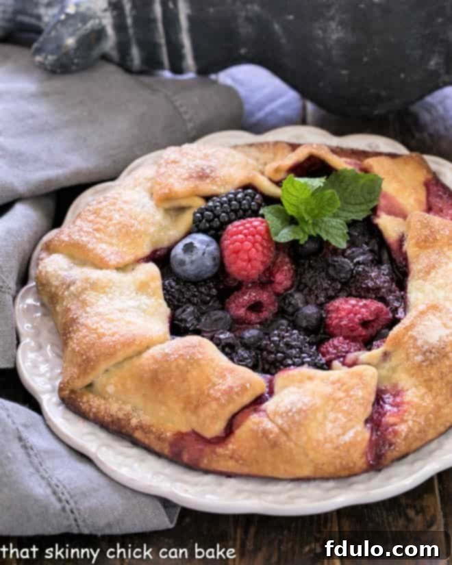 Mixed berry galette with a sprig of mint on a decorative white serving plate.