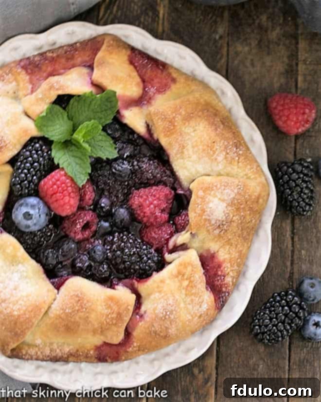 Overhead view of a rustic berry tart on a white plate surrounded by fresh berries.