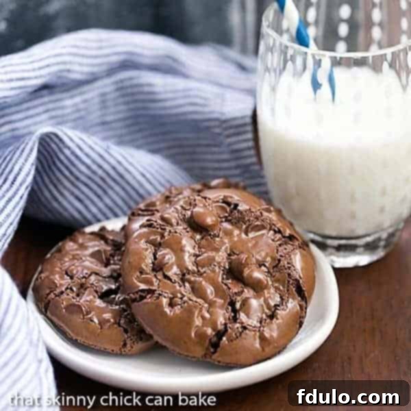 Glossy, rich Flourless Chocolate Cookies piled on a small oval white plate, with a glass of milk in the background.