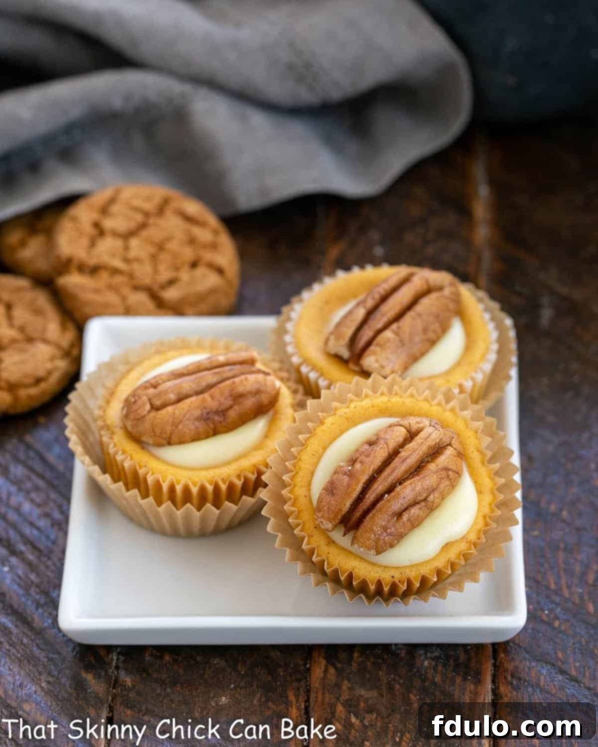 Spiced Pumpkin Cheesecake Cups 4 Three beautifully garnished mini pumpkin cheesecakes presented on a clean, square white plate, ready to be enjoyed.