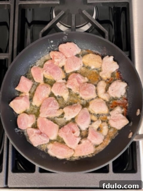 Step 1: Cubed chicken being tossed in a flour mixture on a sheet pan, ready for sautéing.