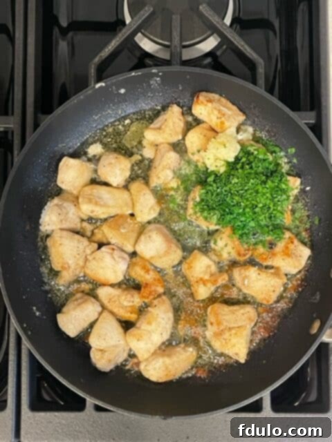 Step 3: Cooked chicken tossed with freshly minced garlic, vibrant parsley, and melting butter in a skillet.